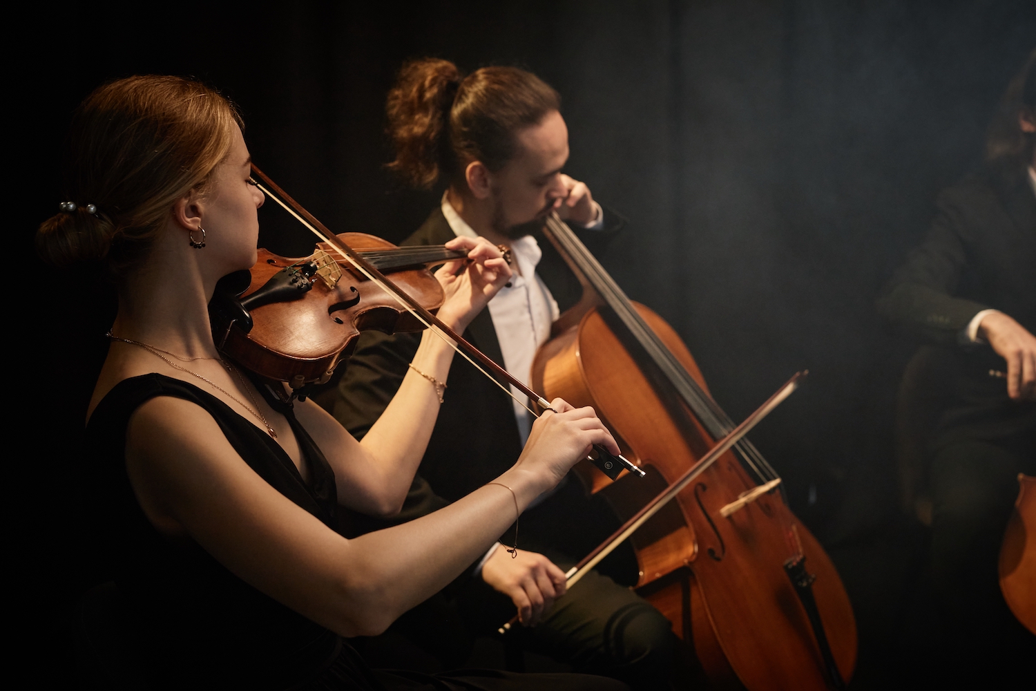 Side view of chamber female and male musicians playing violin and cello with passion during symphonic quartet concert on stage with black curtains